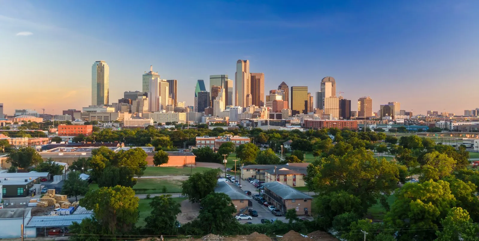 Downtown Dallas, Texas skyline above tree-lined neighborhoods in early evening light