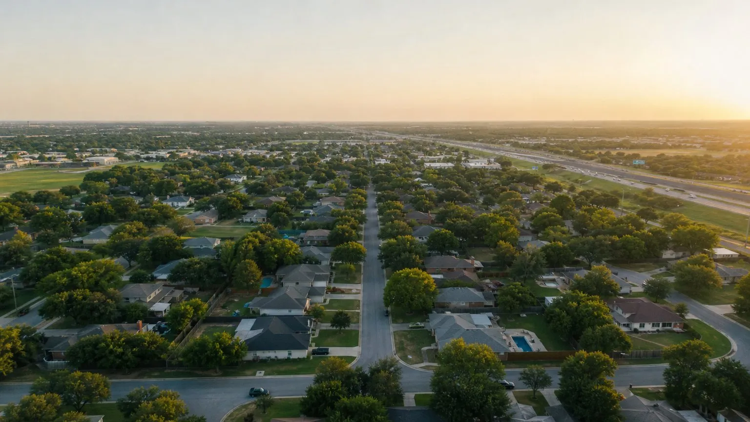 Aerial view of tree-lined Texas suburban streets and a distant freeway at golden hour